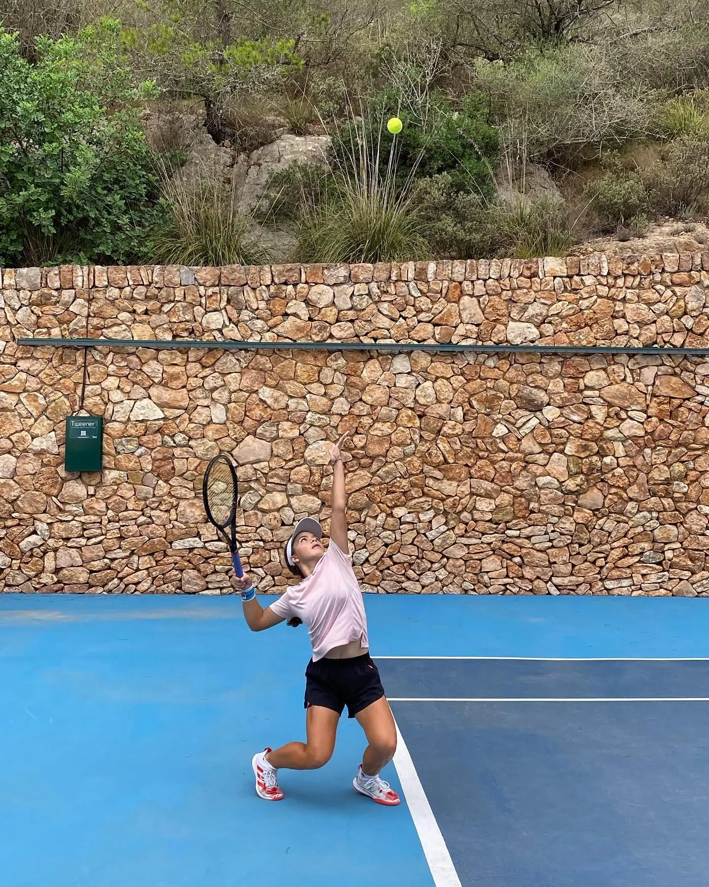 Jeune joueuse à l'entraînement sur le court bleu, mur de pierre sèche derrière