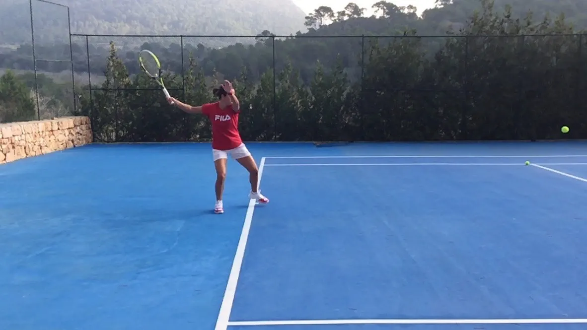 Joueuse à l'entraînement sur le court, collines boisées au fond